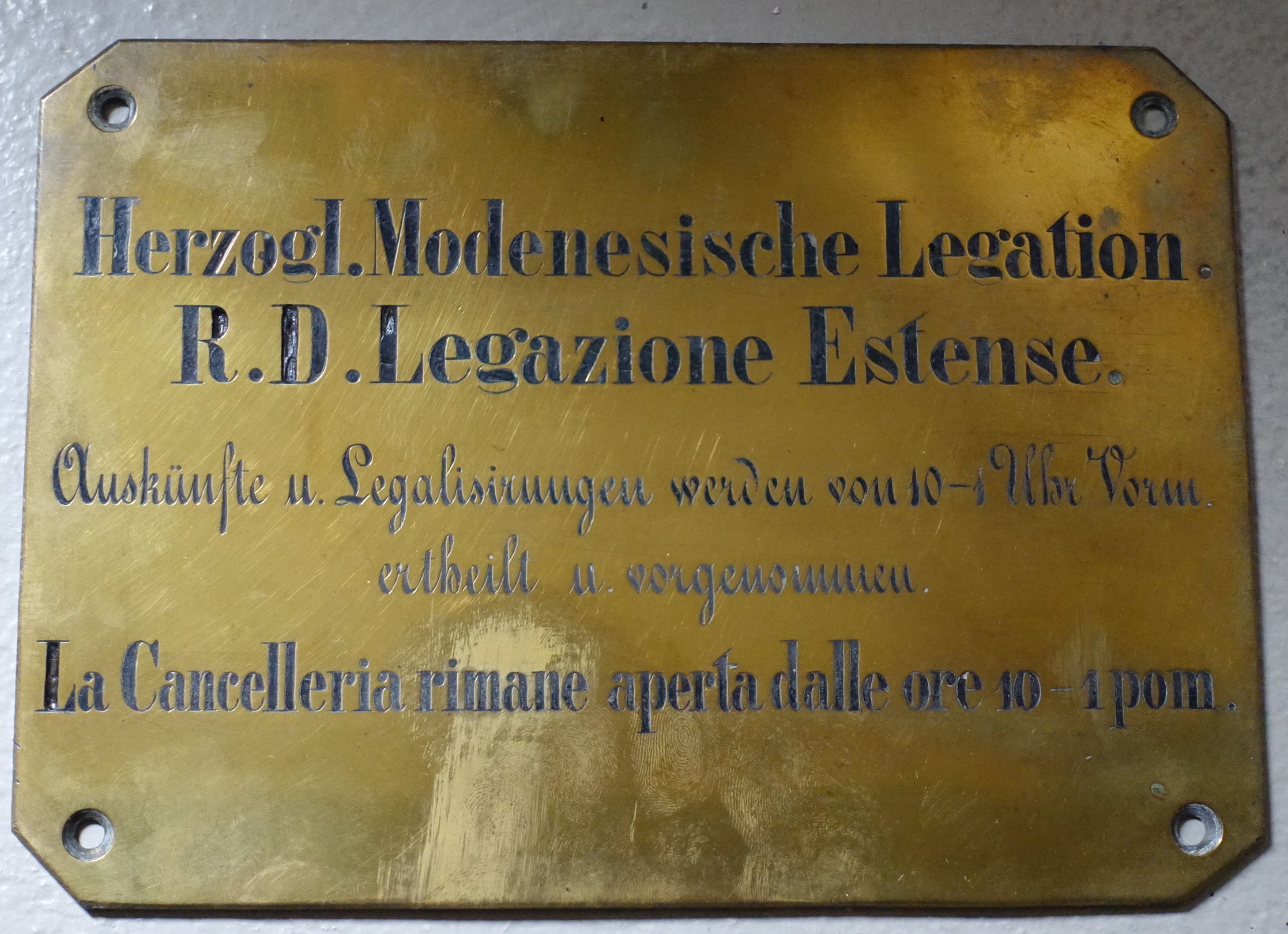 Targa italo-tedesca della Legazione Estense, originariamente affissa al portone d’ingresso del palazzo di Beatrixgasse 29. Si comunica che la Regia Ducale Legazione Estense rilascia informazioni ed effettua legalizzazioni dalle ore 10 all’una. La targa, conservata all’Archivio di Stato di Modena, è uno dei pochi cimeli superstiti del palazzo (foto M. Carfì e V. Soldani, Archivio di Stato di Modena)